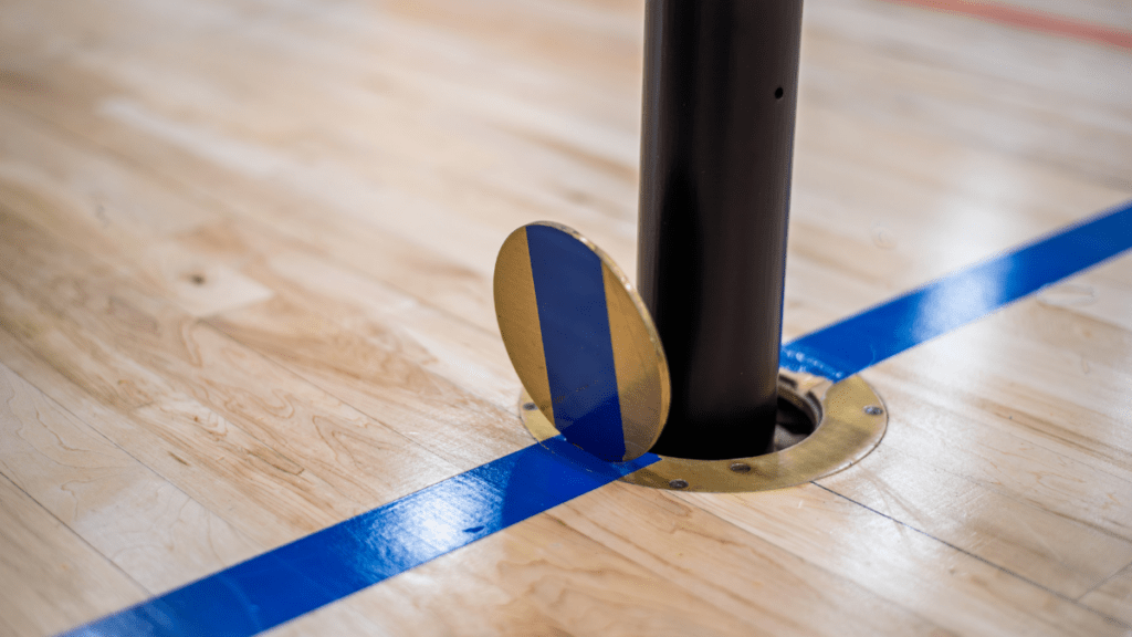 volleyball floorplate installed on gym floor with a volleyball pole inserted